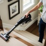 A person using a cordless handheld vacuum cleaner to clean the carpeted treads and edges of an indoor staircase